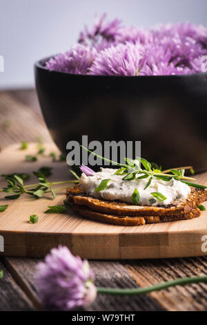 Eine köstliche Knoblauch und Schnittlauch Frischkäse auf herbed Cracker neben einer Schale lila Schnittlauch Blumen. Stockfoto