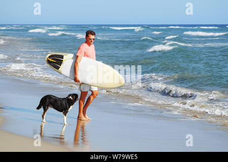 Männliche Surfer am Strand mit einem Hund. Stockfoto