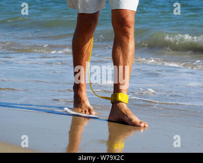 Close-up ein Surfer zu Fuß am Strand entlang auf seinem Fuß eine gelbe Leine. Atlantik. Sandstrand. In shorts gebräunte Beine angezogen. Stockfoto