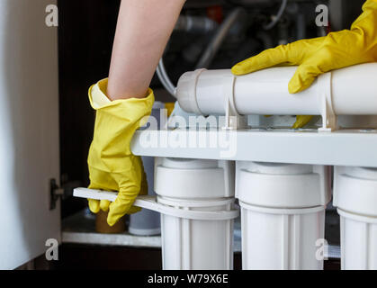 Klempner in gelb Haushaltshandschuhe änderungen Wasser filtern. Handwerker Installation von Wasser Filterpatronen in der Küche. Trinkbares Wasser Filtration System i Stockfoto