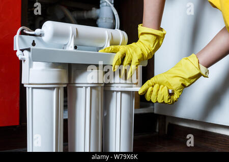 Klempner in gelb Haushaltshandschuhe änderungen Wasser filtern. Handwerker Installation von Wasser Filterpatronen in der Küche. Trinkwasser Filtersystem Stockfoto