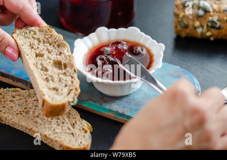 Die Frau ist die Sauerkirschen Marmelade auf dem Brot. Stockfoto