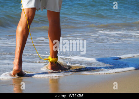 Close-up ein Surfer zu Fuß am Strand entlang auf seinem Fuß eine gelbe Leine. Atlantik. Sandstrand. In shorts gebräunte Beine angezogen. Stockfoto