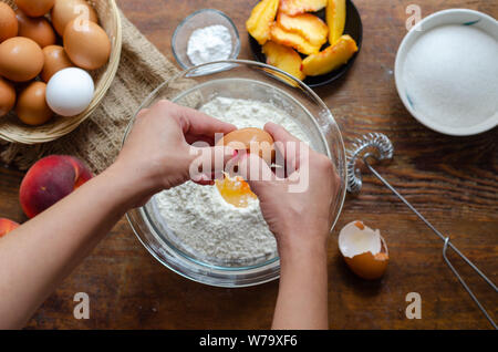 Frau Aufschlagen der Eier in Mehl. Sie bildet (Peach pie. Stockfoto