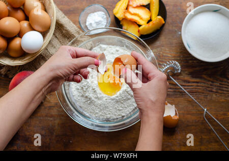 Frau Aufschlagen der Eier in Mehl. Sie bildet Peach pie. Stockfoto