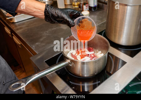 Behandschuhten Koch ist das Hinzufügen von belasteten Tomaten in eine Schüssel, professionelle Küche Stockfoto