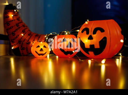 Kinder Beine in stilvollen warmen hellen bunt gestreiften lustige Socken in der girlande Lichter am Boden mit Kürbissen im Zimmer. Die Einrichtung für Halloween, gemütliche Moment. Stockfoto