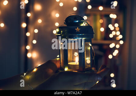 Zicklein hält Weihnachten Laterne in der Hand und leuchtet bokeh Hintergrund. Neues Jahr feier Konzept, festliche Stimmung Stockfoto