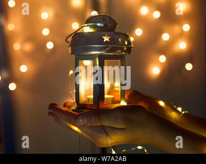 Zicklein hält Weihnachten Laterne in der Hand und leuchtet bokeh Hintergrund. Neues Jahr feier Konzept, festliche Stimmung Stockfoto