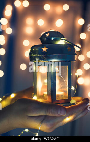 Zicklein hält Weihnachten Laterne in der Hand und leuchtet bokeh Hintergrund. Neues Jahr feier Konzept, festliche Stimmung Stockfoto