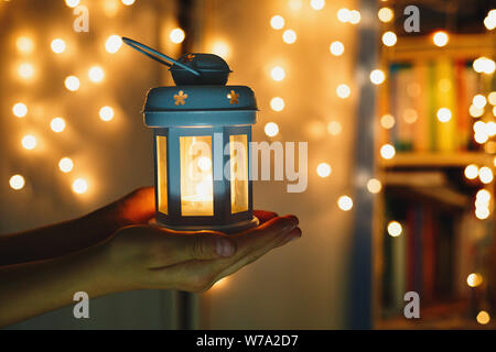 Zicklein hält Weihnachten Laterne in der Hand und leuchtet bokeh Hintergrund. Neues Jahr feier Konzept, festliche Stimmung Stockfoto