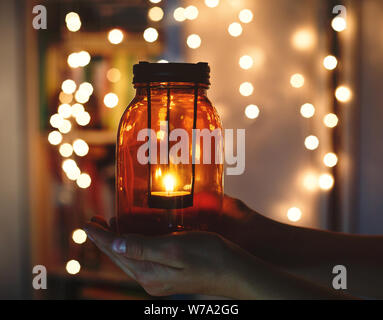 Zicklein hält Weihnachten Laterne in der Hand und leuchtet bokeh Hintergrund. Neues Jahr feier Konzept, festliche Stimmung Stockfoto