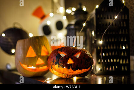 Orange Kürbisse mit unheimlichen Gesichter und Kerzen liegt auf dem Tisch dunklen Hintergrund. Halloween Feier, Home Decoration Konzept Stockfoto