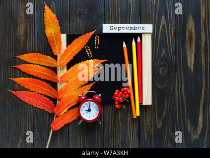 Schiefertafel mit Wecker, rote Blätter auf es auf hölzernen dunklen Hintergrund. Bildung, zurück in die Schule, Herbst, Jahreszeit ändern Konzept Stockfoto