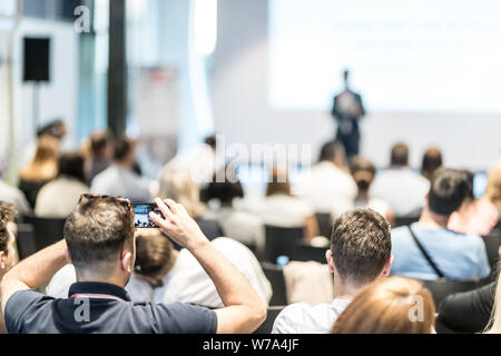 Männliche business Lautsprecher, einen Vortrag an der Konferenz. Ansicht der Rückseite des unbekannter Teilnehmer im Publikum unter Foto Präsentation. Stockfoto