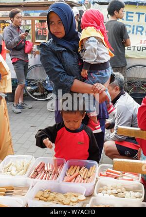 Ein Junge, ein Mädchen und ihre Mutter vor Kunststoffbehältern in einem Street Food stall. Stockfoto