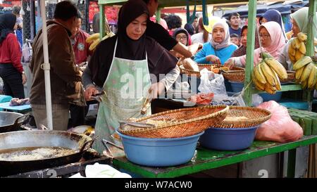 Jakarta, Indonesien - August 2019: Eine muslimische Frau sind braten Bananen zu verkaufen, während die Käufer warten. Stockfoto