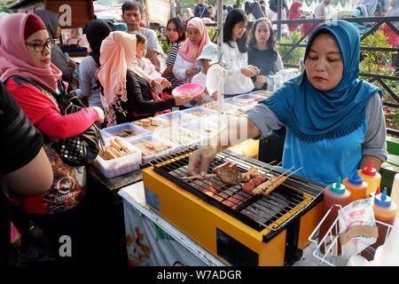 Jakarta, Indonesien - August 2019: Eine muslimische Frau grillen Würstchen zu verkaufen, während die Käufer warten. Stockfoto