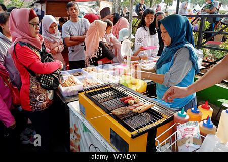 Jakarta, Indonesien - August 2019: Eine muslimische Frau grillen Würstchen zu verkaufen, während die Käufer warten. Stockfoto