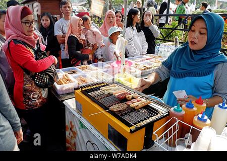 Jakarta, Indonesien - August 2019: Eine muslimische Frau grillen Würstchen zu verkaufen, während die Käufer warten. Stockfoto