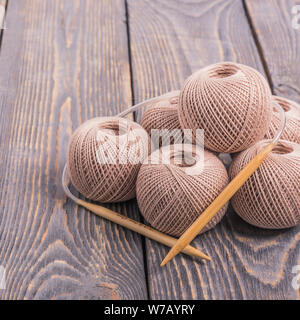 Kugeln von Garn und Stricknadeln zum Stricken auf einer hölzernen Hintergrund Stockfoto