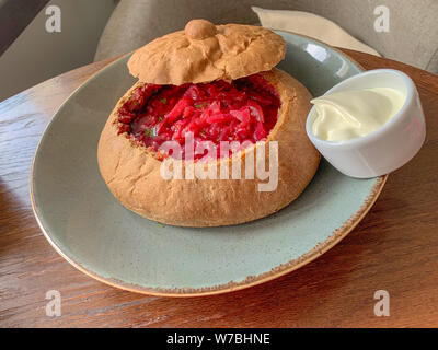 Traditionelle russische und ukrainische Suppe Borschtsch. Borsch ist im Brot statt einer Platte serviert. In der Nähe von einem Teller mit saurer Sahne. Stockfoto