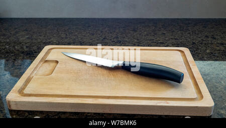 Seitenansicht eines isolierten Schälmesser auf einem grossen hölzernen Schneidebrett mit Granit Arbeitsplatte in der Küche top Hintergrund Stockfoto