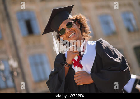 Fröhliche Junge sein Diplom umarmen in der Hochschule Hof. Stockfoto