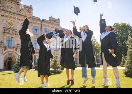 Absolventen springen hoch mit den Kappen. Stockfoto