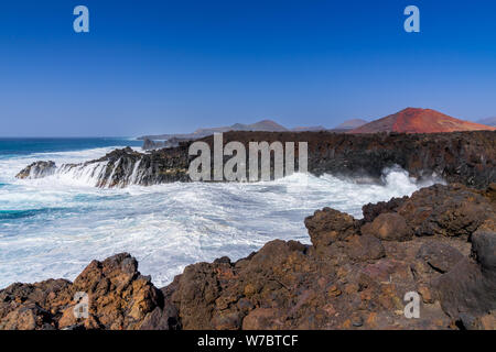 Spanien, Lanzarote, rauen Atlantik in Los Hervideros cove Neben rote Vulkane Stockfoto