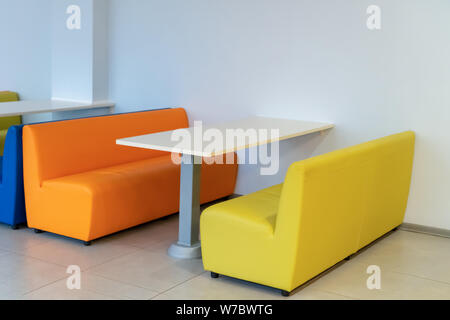 Russland, Tatarstan, 13. April 2019. Zwei bunte Sessel Sofas mit einem Tisch im Zimmer. Gelb und Orange Bänken. Interior Design. Schule. Stockfoto