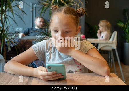 Russland, Tatarstan, 13. April 2019. Ein jugendlicher Mädchen in einem Restaurant schaut in ein iPhone XS und ist überrascht. Mund schließt seine Hand in der Überraschung. Resta Stockfoto