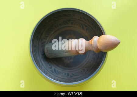 Klangschale close-up, beruhigend und meditativ. Klangschale mit Sanskrit Gravur Muster und Holzhammer auf gelbem Hintergrund Stockfoto