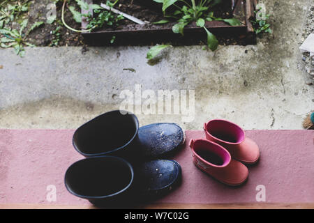 Zwei Gummistiefel Paare (Vater und Tochter) auf der Veranda am Eingang des Hauses während eines regnerischen Tag Stockfoto