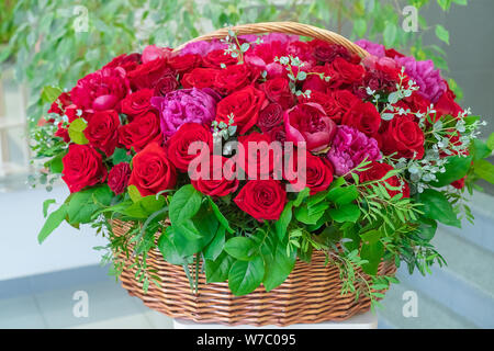 Lieferung von einem Blumenstrauß im Büro. Ein großer Blumenstrauß aus Rosen und Pfingstrosen in einem grossen Korb. Rote Rosen und rosa Pfingstrosen in einem braunen Korb. Stockfoto