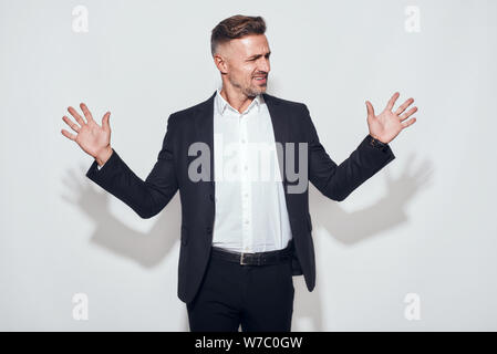 Hoppla. Porträt von unglücklichen bärtigen Geschäftsmann breitet Hände mit unzufriedenen Ausdruck, während vor grauem Hintergrund stehen. Negative Emotionen. Geschäftskonzept Stockfoto