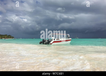 Dominikanische Republik, Punta Cana. Juni 29, 2016. Karibische Meer vor dem Regen. Boot mit zwei Personen am Ufer vertäut. Wolken. Türkisblaues Wasser. Stockfoto