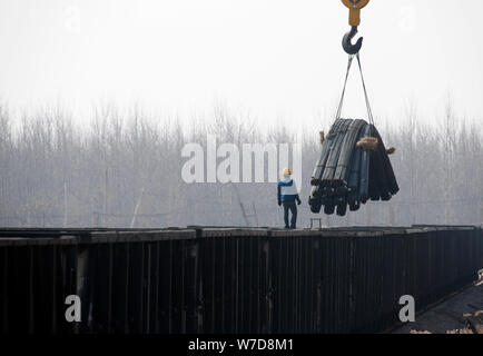 ---- Ein chinesischer Arbeiter leitet einen Kran, ein Zug mit Stahlrohre in Stadt Huaibei zu laden, der ostchinesischen Provinz Anhui, 13. März 2014. Chinas BIP r Stockfoto