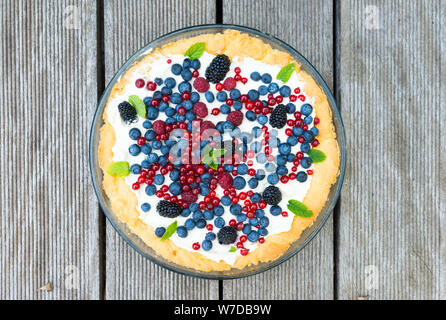 Törtchen mit frischen Blaubeeren, Himbeeren, Brombeeren, Johannisbeeren und Sahne mit Minze dekoriert. Ansicht von oben Stockfoto