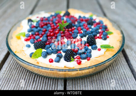 Törtchen mit frischen Blaubeeren, Himbeeren, Brombeeren, Johannisbeeren und Sahne mit Minze dekoriert. Ansicht von oben Stockfoto