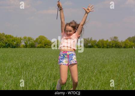 Glückliches Mädchen mit langem Haar mit einem farbigen Mühle Spielzeug in die Hände erhebt ihre Hand und springt. Konzept der Sommer, Freiheit und glückliche Kindheit. Conce Stockfoto