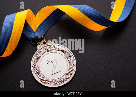 Den zweiten Platz Runner-up Silber Medaille auf eine Zwirbelte Blau und Gold Ribbon über ein dunkelgrauer Hintergrund mit Kopie Raum von oben gesehen Stockfoto