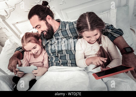 Zwei Schwestern noch im Bett spielen am Telefon mit ihren Papa im Bett Stockfoto