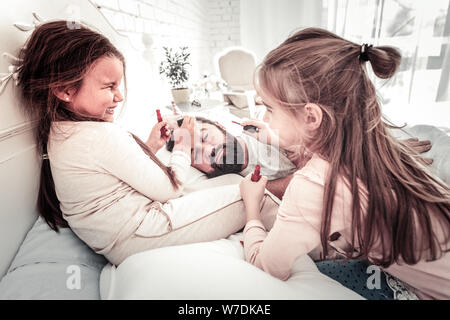 Süße Schwestern auf ihren Papa Gesicht, während er schläft Stockfoto