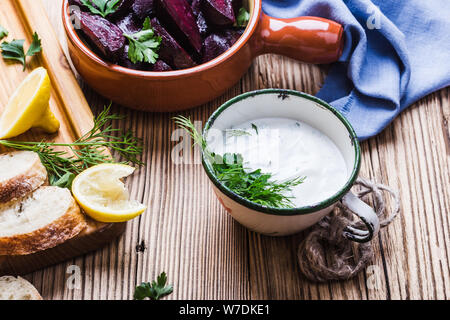 Joghurt Dip mit Petersilie, Dill und Zitronensaft auf rustikalen Holztisch mit gerösteten Rüben, Brot und frische Zitrone Wasser serviert, Nahaufnahme, vegan Anlage bas Stockfoto