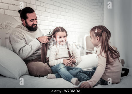 Vater, der seine Kinder Zöpfe sitzen auf dem Bett Stockfoto