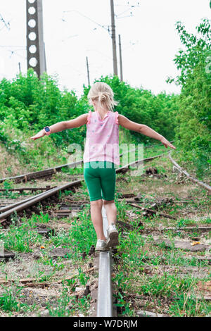 Das kleine Mädchen geht auf den alten, verlassenen Eisenbahnen Stockfoto