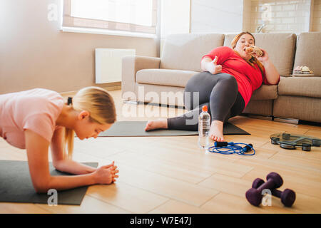 Schnittansicht der Jungen schlanken Frau in Ganzkörperstütz. Fett Körper positives Modell lehnte sich auf Sofa und Burger essen. Wie Symbol. Plus Size mod Stockfoto