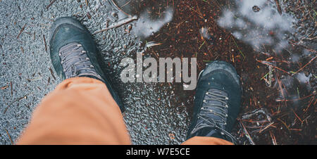 Mann staingg während der regnerischen Herbst Wetter in eine Pfütze in einem wasserdichten tracking Schuhe. Herbst wetter Konzept. All Season adventure Konzept. Muddy backgrou Stockfoto