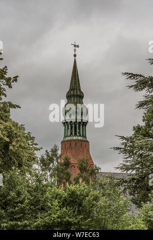 Ein Kupfer Turmspitze auf einem zwiebelturm unter den grünen Bäume gegen eine graue Himmel bei Frederiksvarek, Dänemark, 30. Juli 2019 Stockfoto